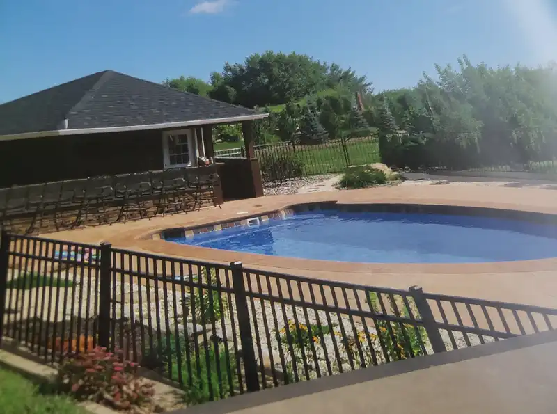 Black aluminum pool safety fence with self-closing gate around an in-ground pool